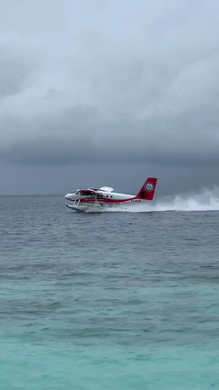 Ein rot-weißes Wasserflugzeug gleitet vor grauen Wolken über das Meer und zieht eine weiße Gischtspur.