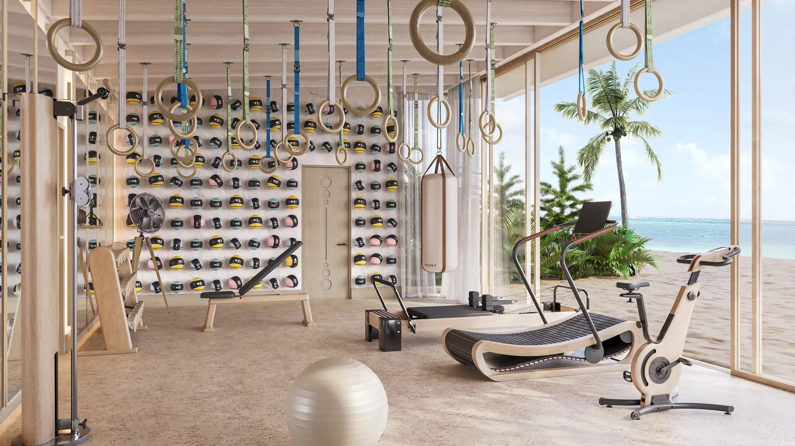 Eine Visualisierung zeigt einen Fitnessraum mit hängenden Turnringen, einer Wand voller Medizinbälle, Laufband, Reformer und Ergometer, rechts eine Glaswand zu Strand und Palmen