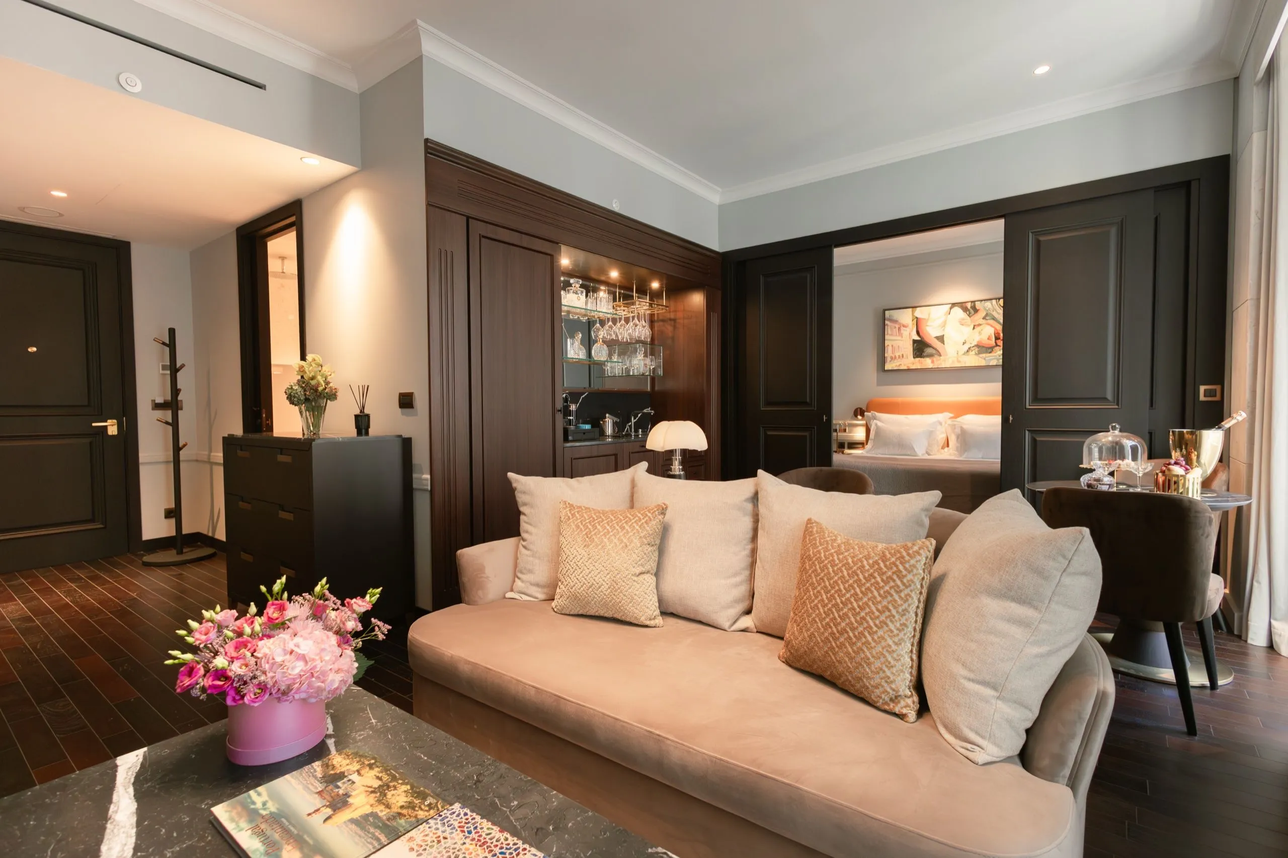 Wohnbereich einer MYTHIC Suite mit heller Couch, dunklem Holz und Blick ins Schlafzimmer.